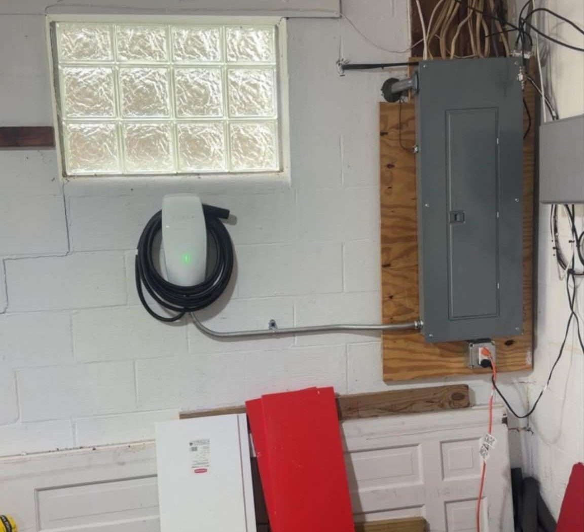 A wall-mounted EV charger with its cable coiled, with conduit run over to the electrical panel in a garage