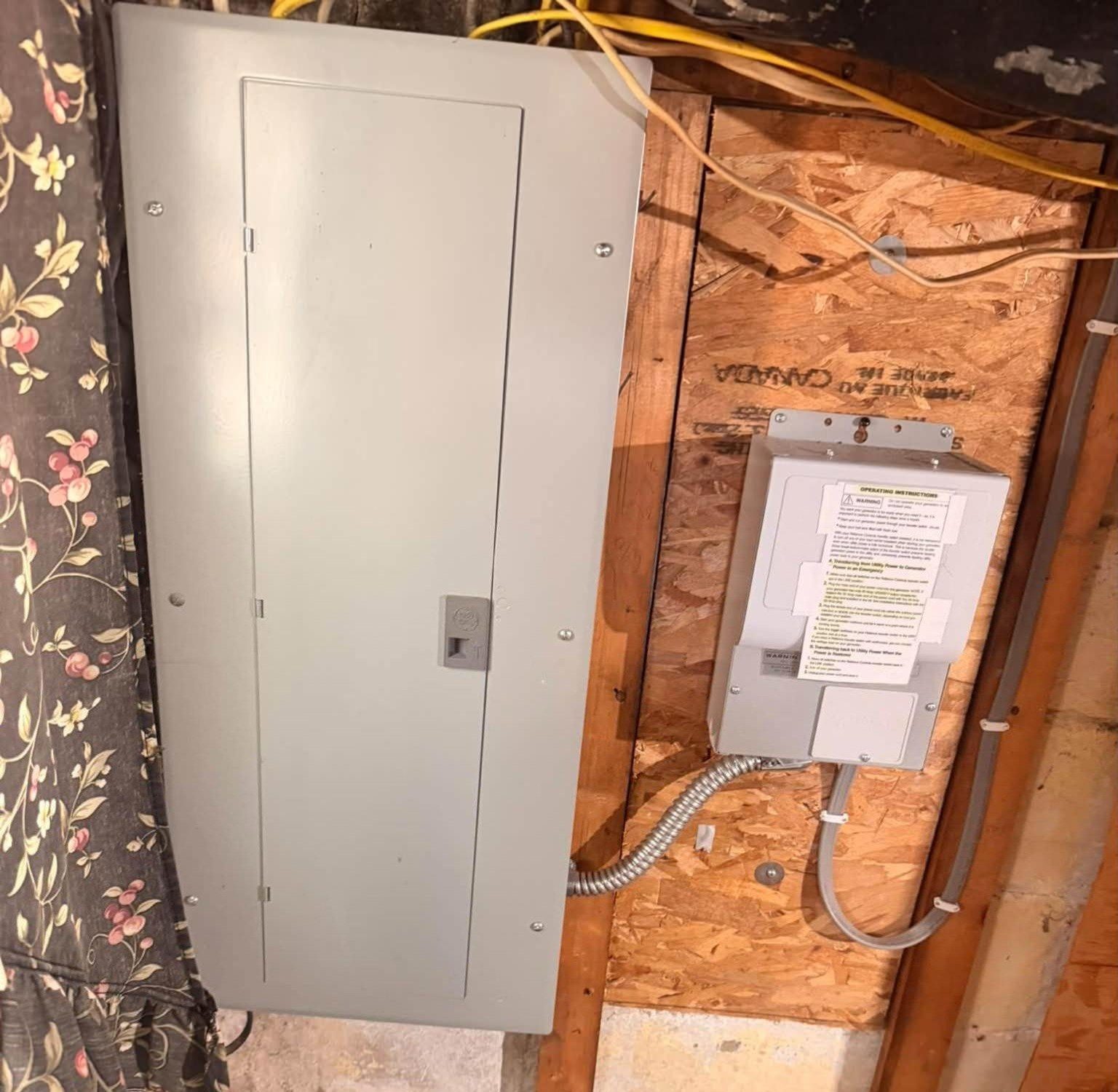 A new electrical panel beside a switch box on an OSB board in a basement