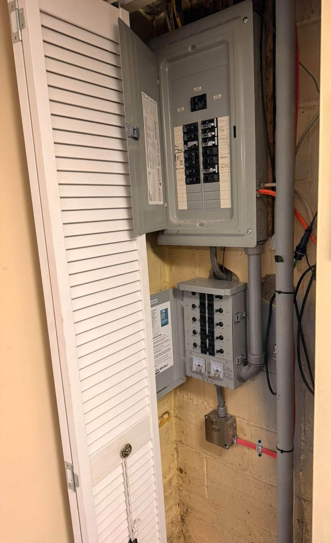 A main breaker panel with a switch box mounted below it in a utility closet